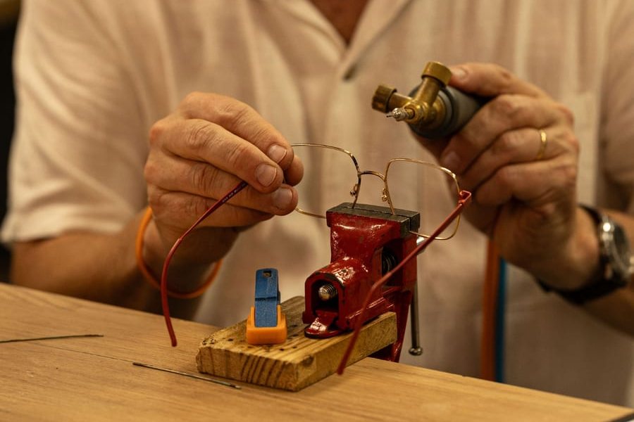 Frédéric ressoude une monture métal maintenue dans un étau, chalumeau à la main, à l'atelier de Gravelines Optique