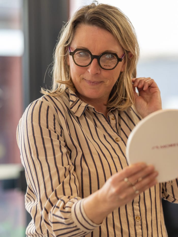 Cliente essayant des lunettes de vue rondes devant un miroir — Gravelines Optique, Montivilliers