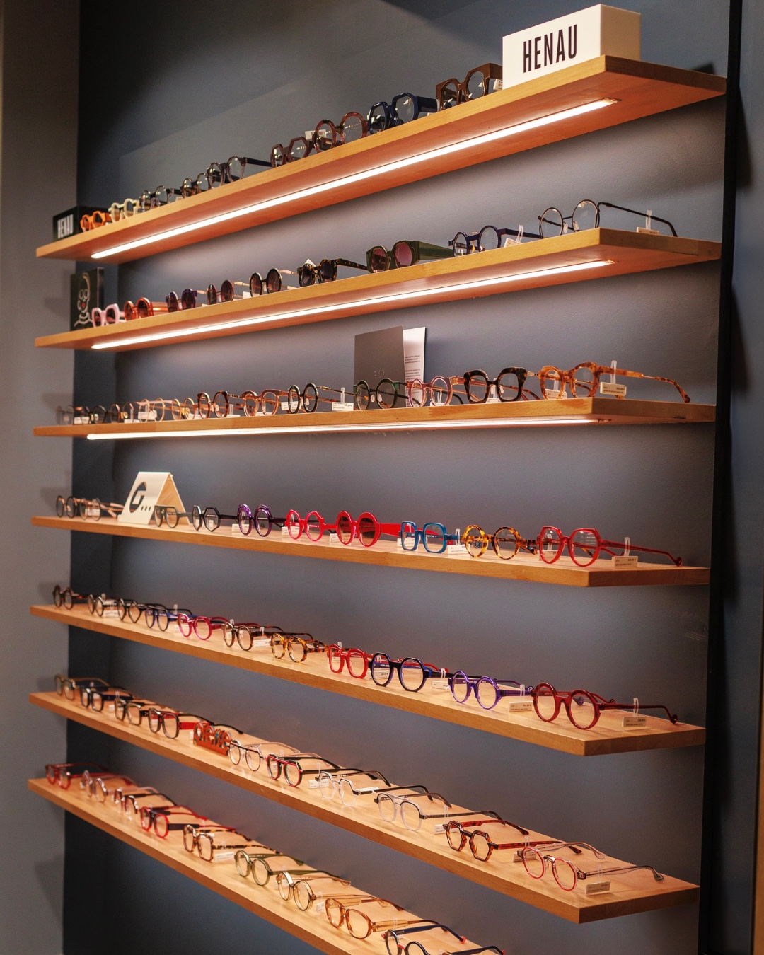 Le mur de montures de la boutique, présentées sur des étagères de bois éclairées