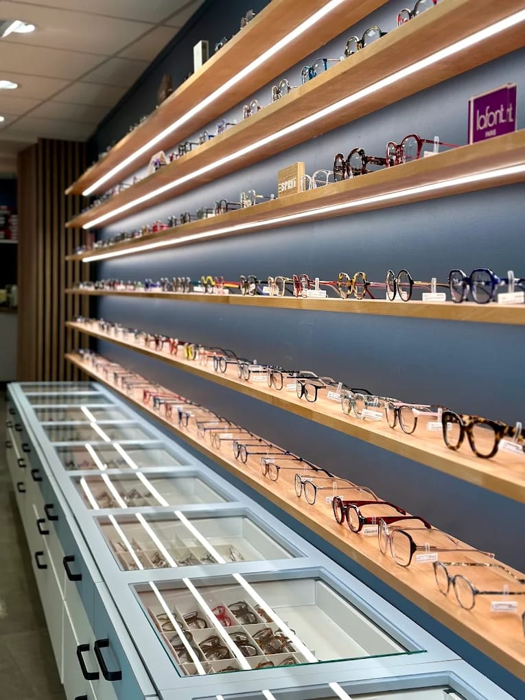 Mur de montures de la boutique Gravelines Optique à Montivilliers, présentées sur étagères de bois éclairées